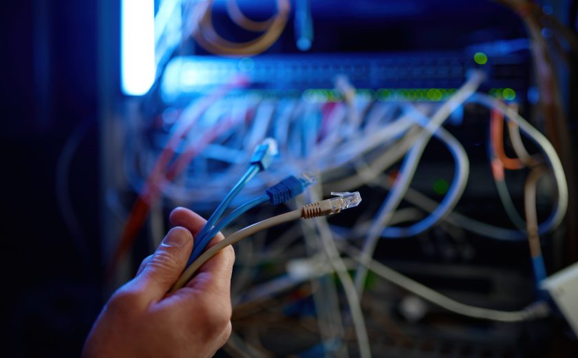 Cropped closeup shot of hand connecting cables to network server in server room or data center for maintenance. Technology, connection and wires concept